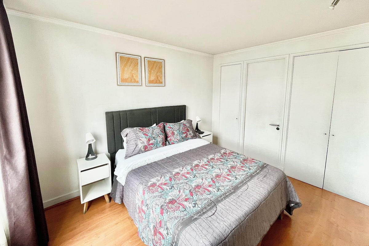 A bedroom with a bed, a nightstand, a wardrobe, and two framed pictures on the wall.