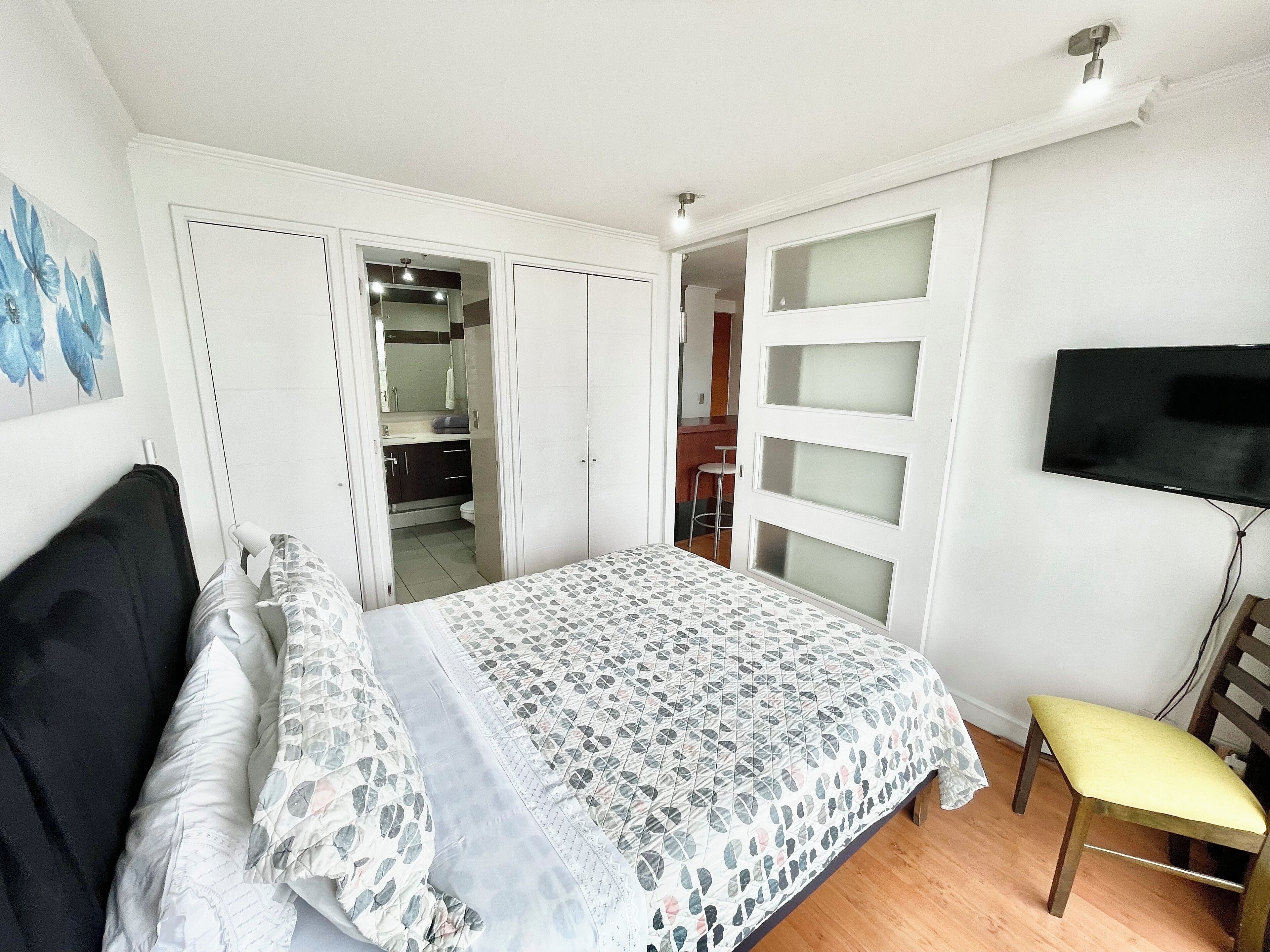 Un dormitorio con cama, una silla, un televisor y un armario.
