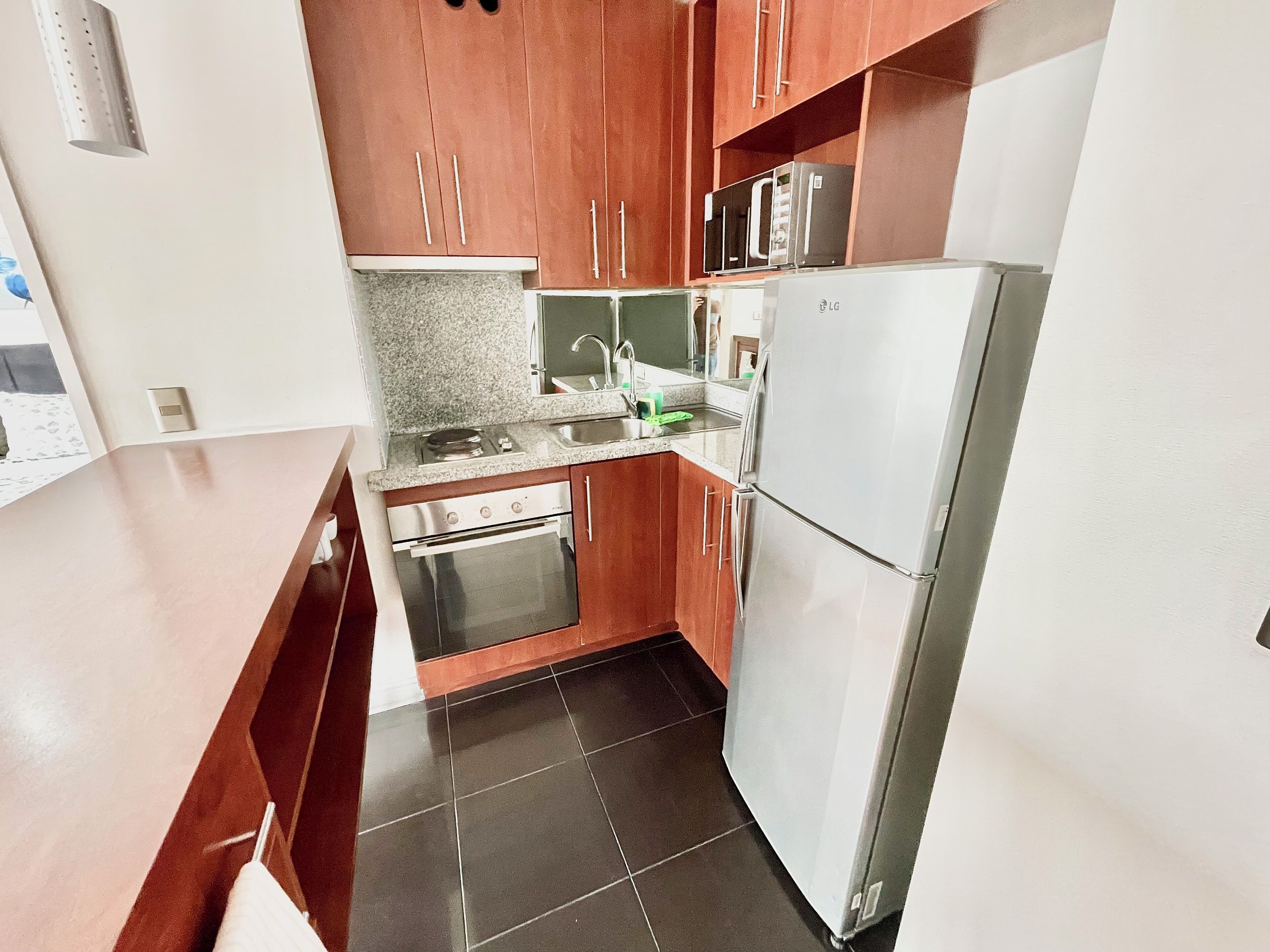 Una cocina compacta con armarios de madera, un refrigerador de acero inoxidable, un horno y una encimera de granito.