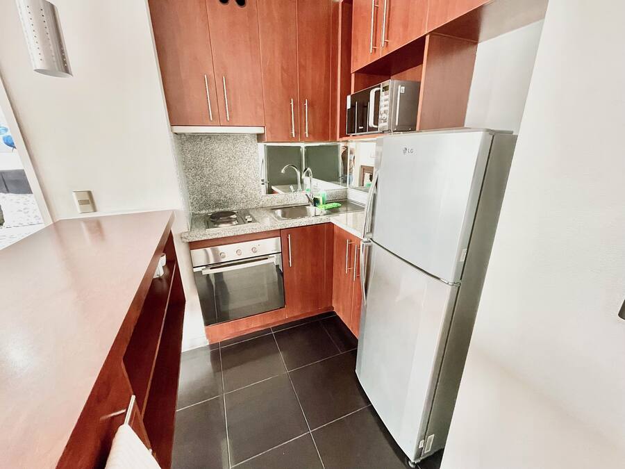 Una cocina compacta con armarios de madera, un refrigerador de acero inoxidable, un horno y una encimera de granito.
