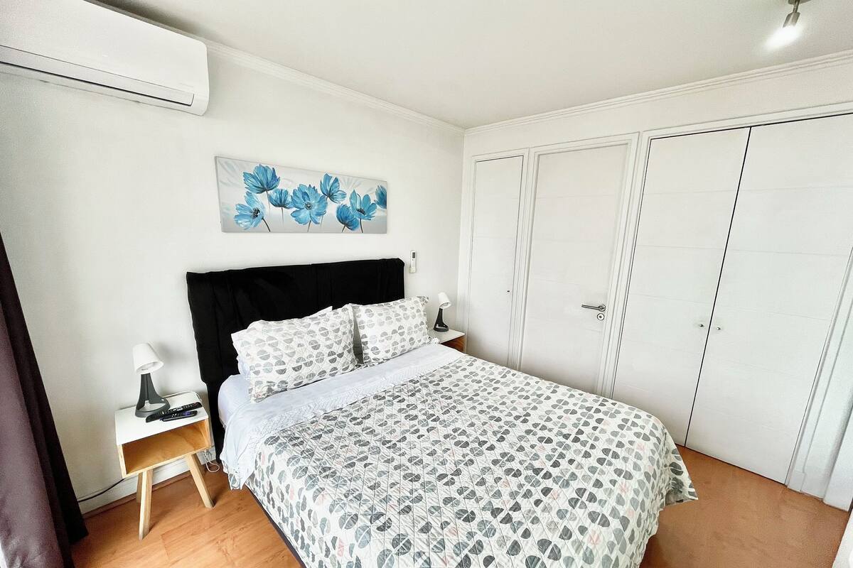 A bedroom with a bed, a nightstand, a lamp, a painting, and a wardrobe.