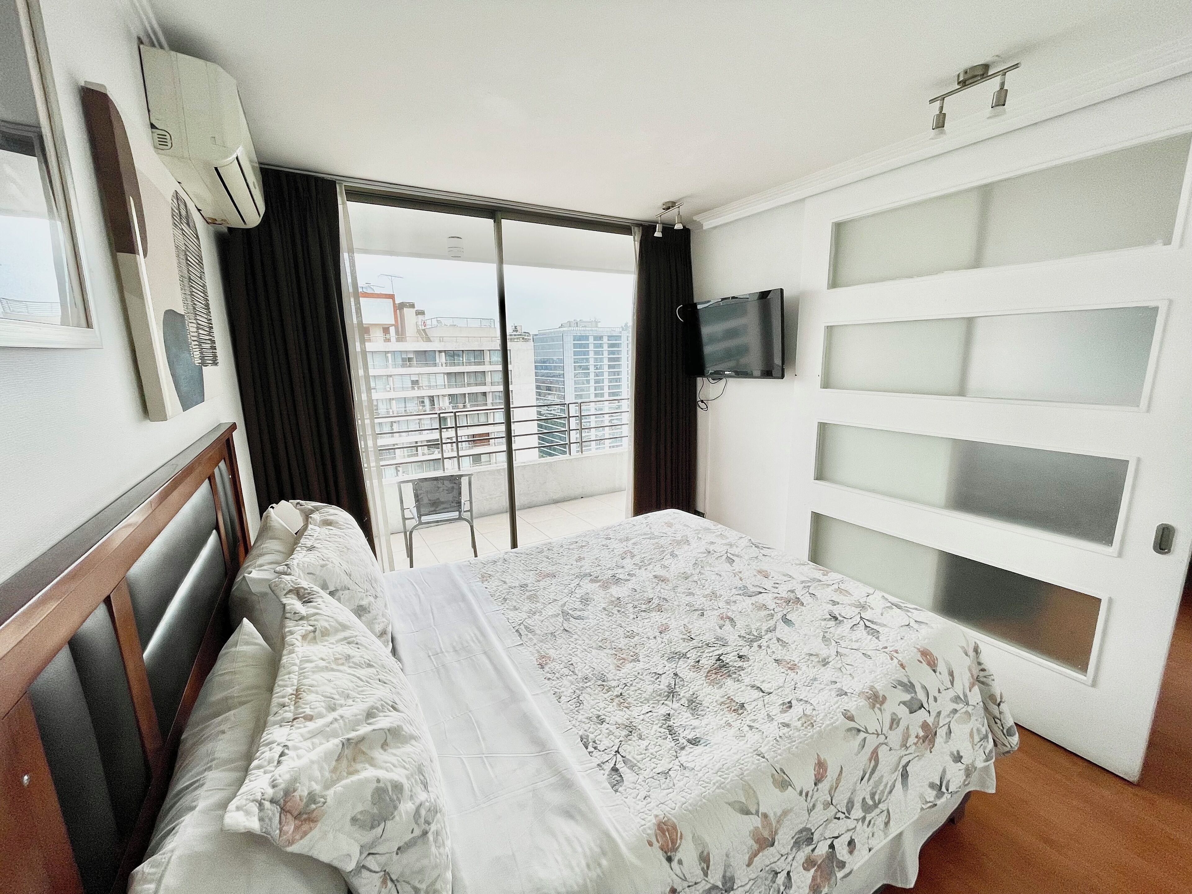 Een hotelkamer met een bed, een aan de muur bevestigde televisie en een balkon met uitzicht op de stad.