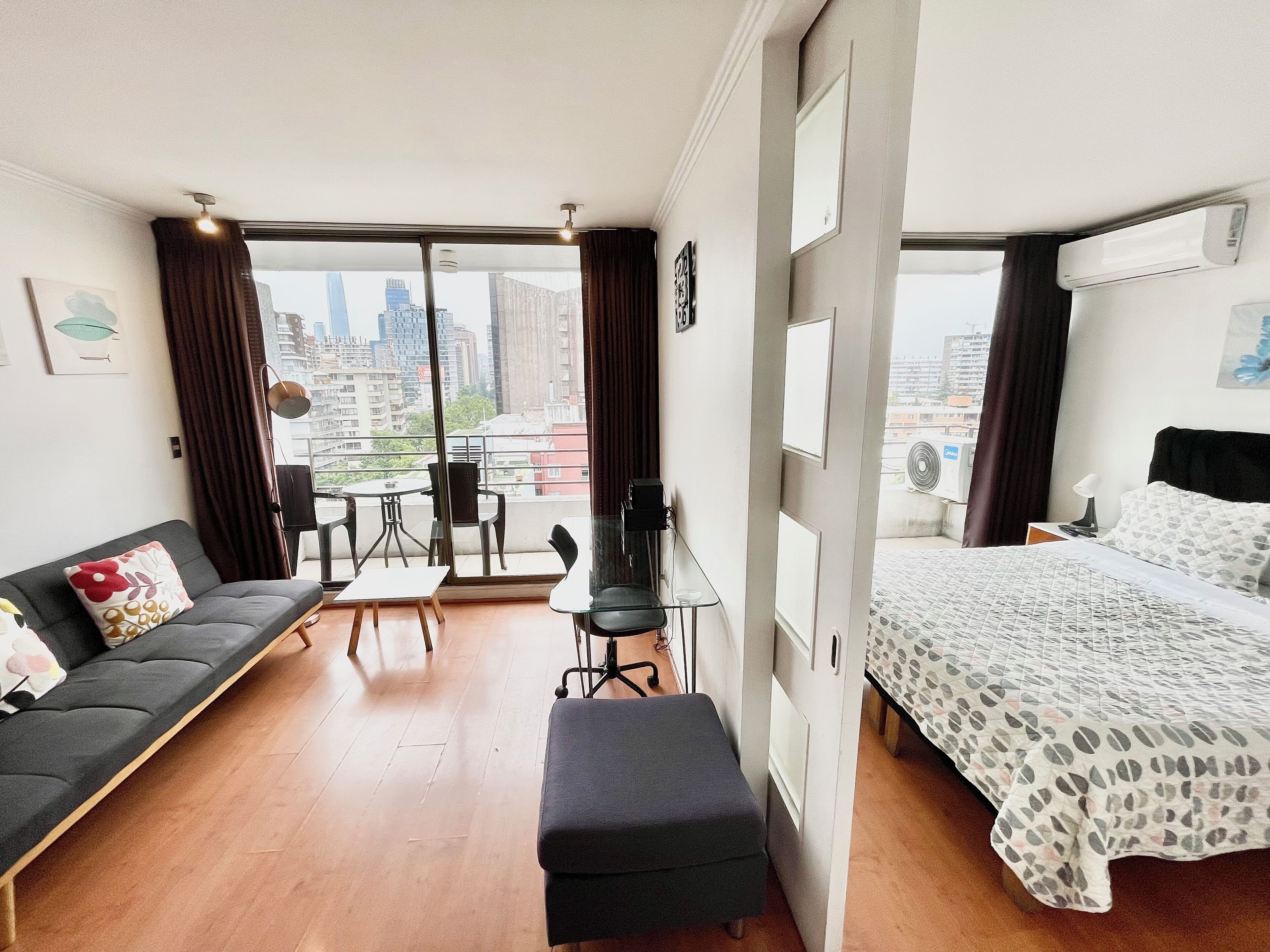 A modern hotel room with a balcony, a sofa, a bed, a desk, and a chair.