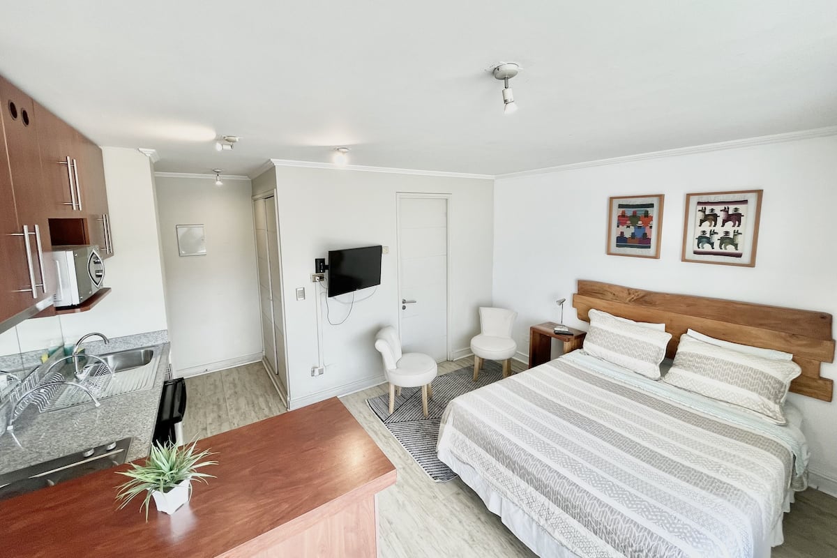 A modern hotel room with a bed, a desk, a TV, and a bathroom.