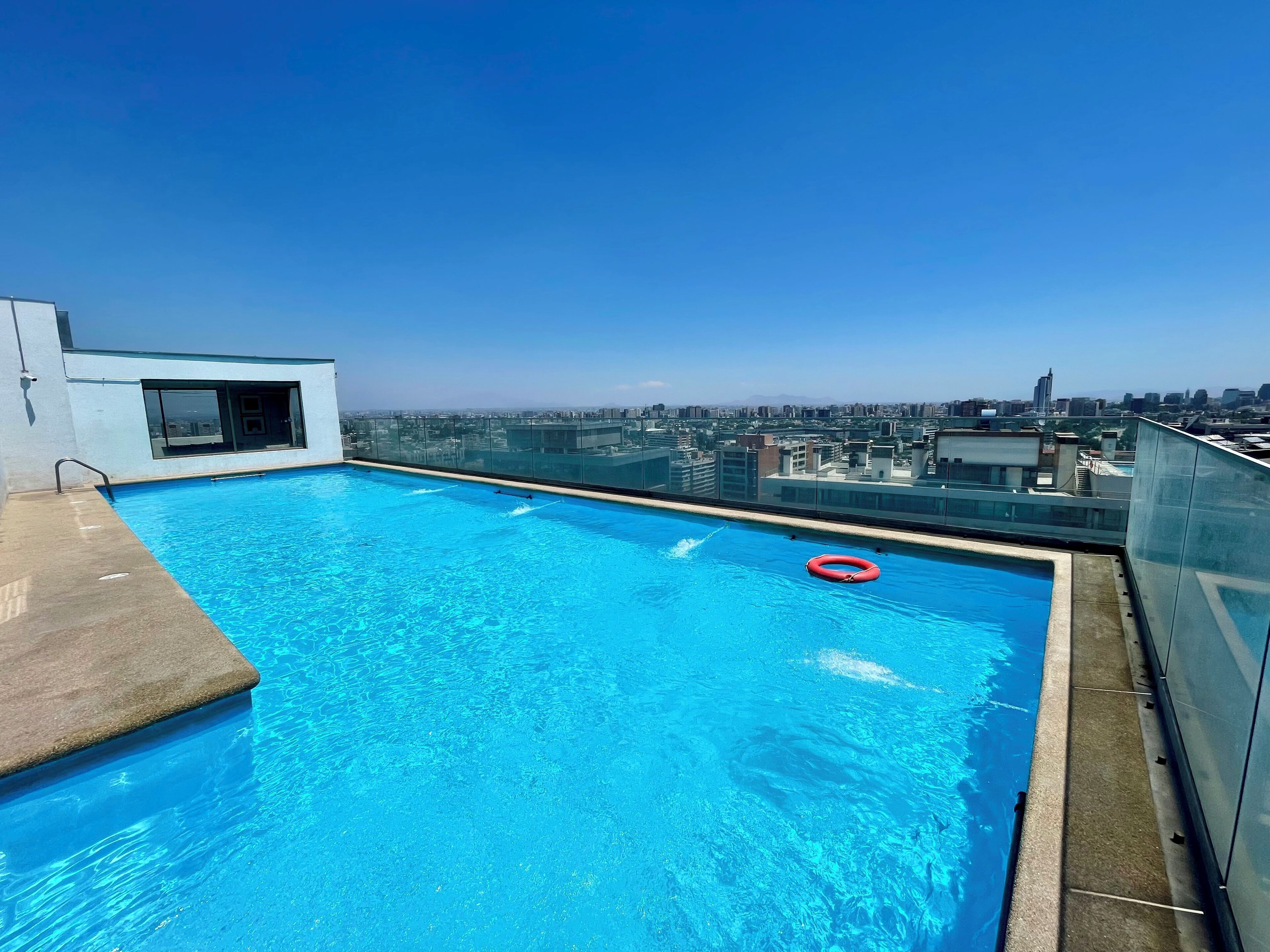 Une piscine sur le toit, avec une eau d’un bleu limpide, un flotteur rouge et une vue sur la ville en arrière-plan.