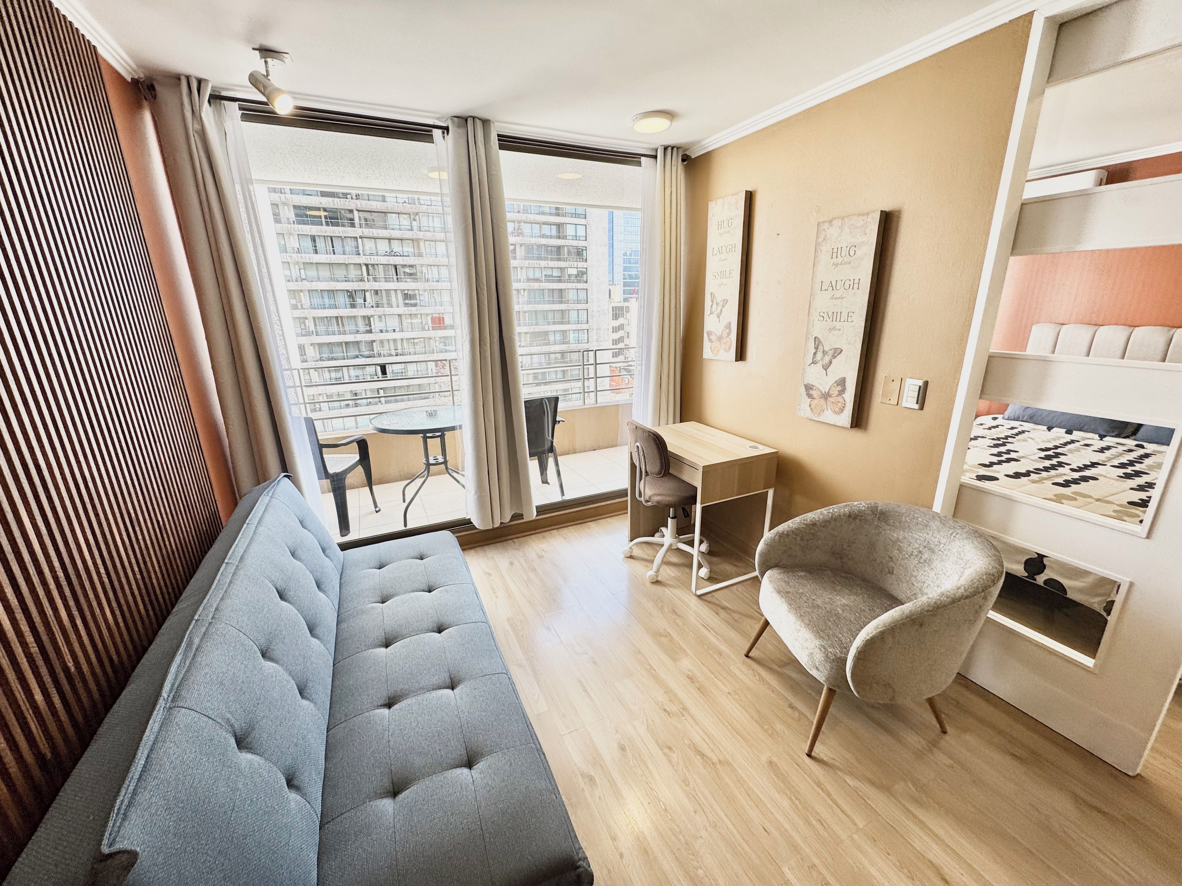 Una sala de estar moderna con sofá, escritorio, silla y vista a la ciudad a través de amplios ventanales.