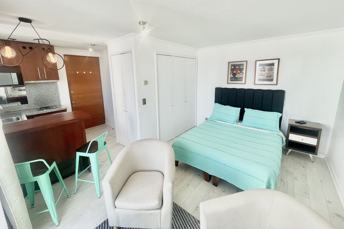 A compact bedroom with a bed, bedside table, and a small kitchenette.