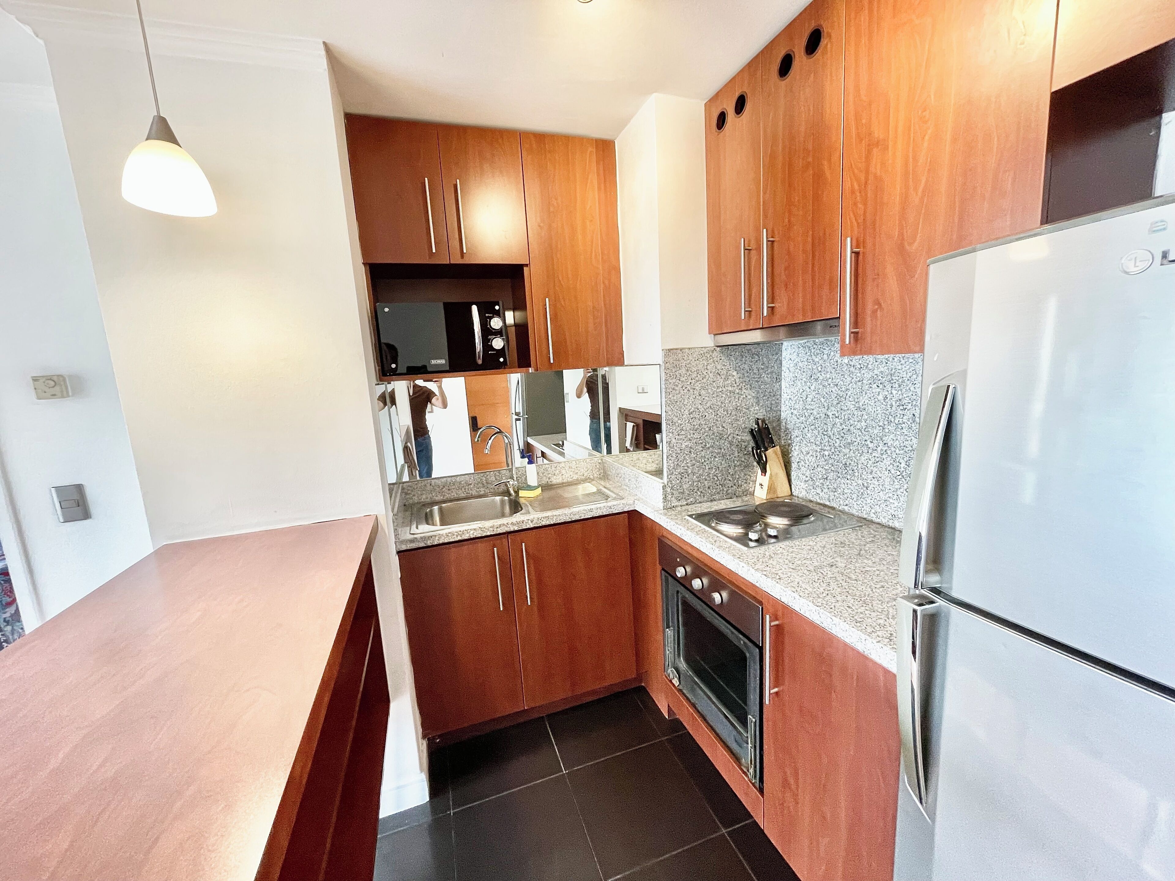 A modern kitchen with wooden cabinets, a stainless steel refrigerator, a built-in oven, and a granite countertop.