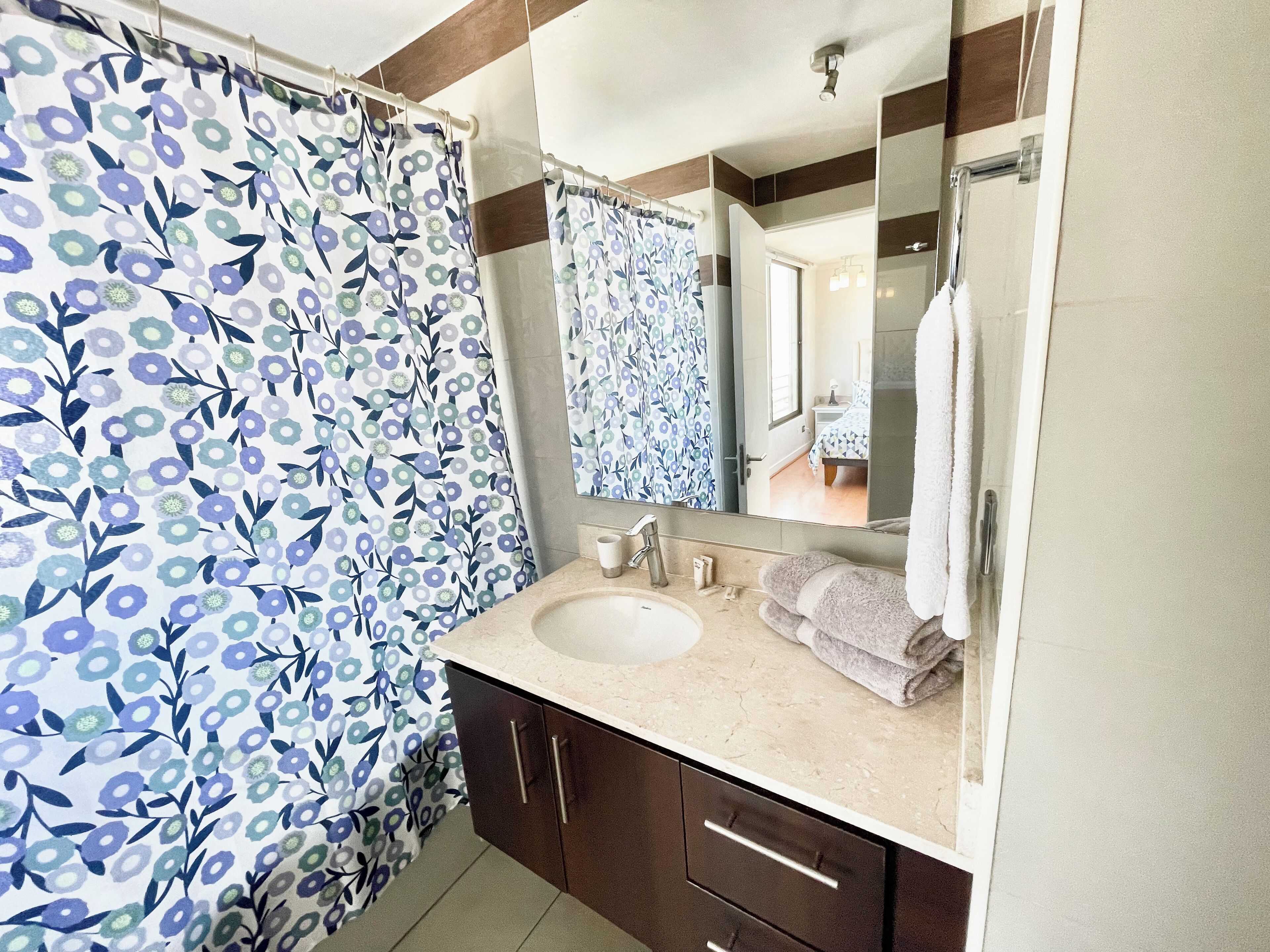 A bathroom with a floral shower curtain, a sink with a mirror, and a towel rack.