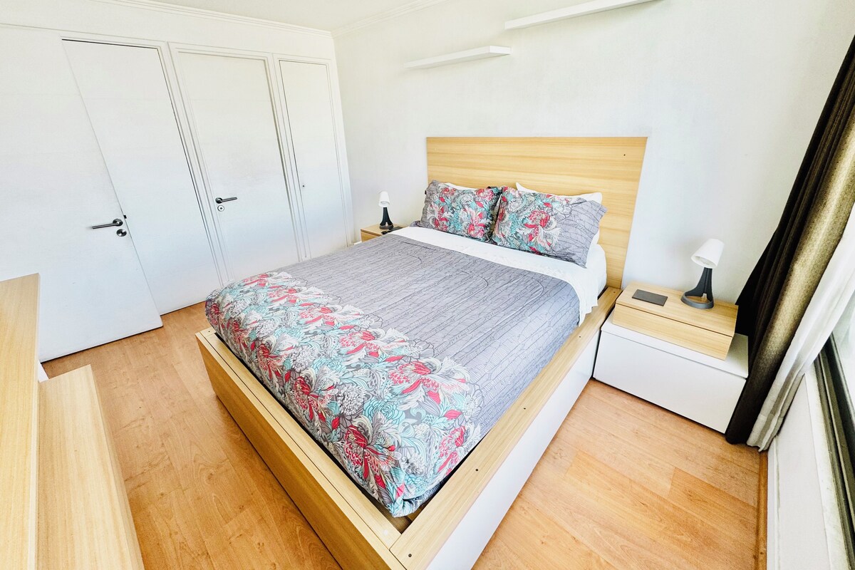 A bedroom with a bed, bedside tables, a wardrobe, and a window with curtains.
