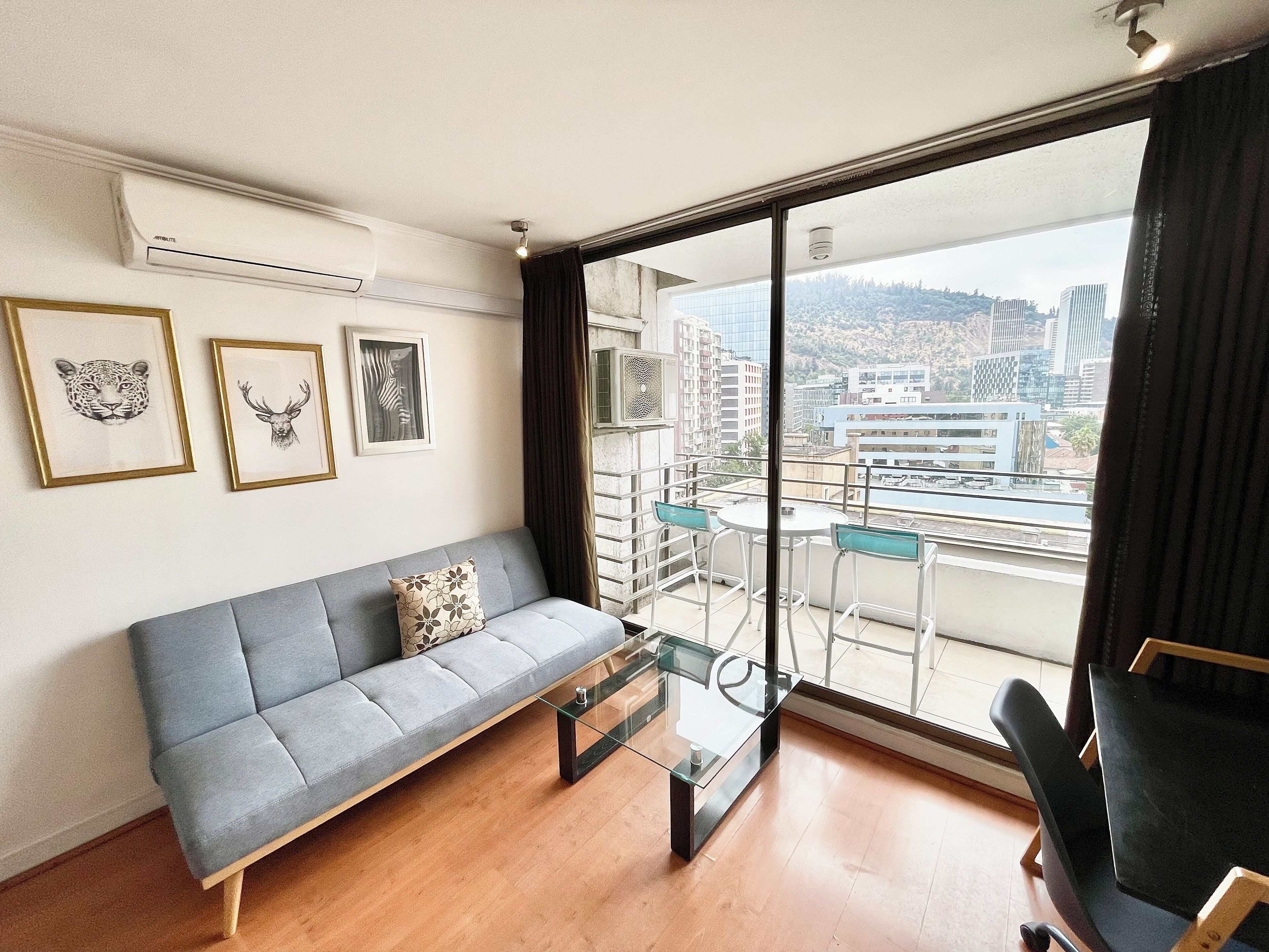 Ein modernes Wohnzimmer mit einem grauen Sofa, einem Glastisch und einem Balkon mit Stadtblick.