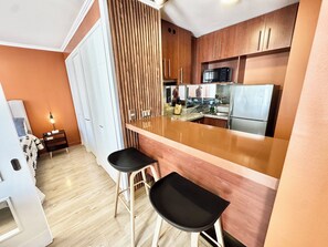 A compact kitchen with a wooden countertop, two black bar stools, a microwave, and a refrigerator. - Rho.cl (Santiago)