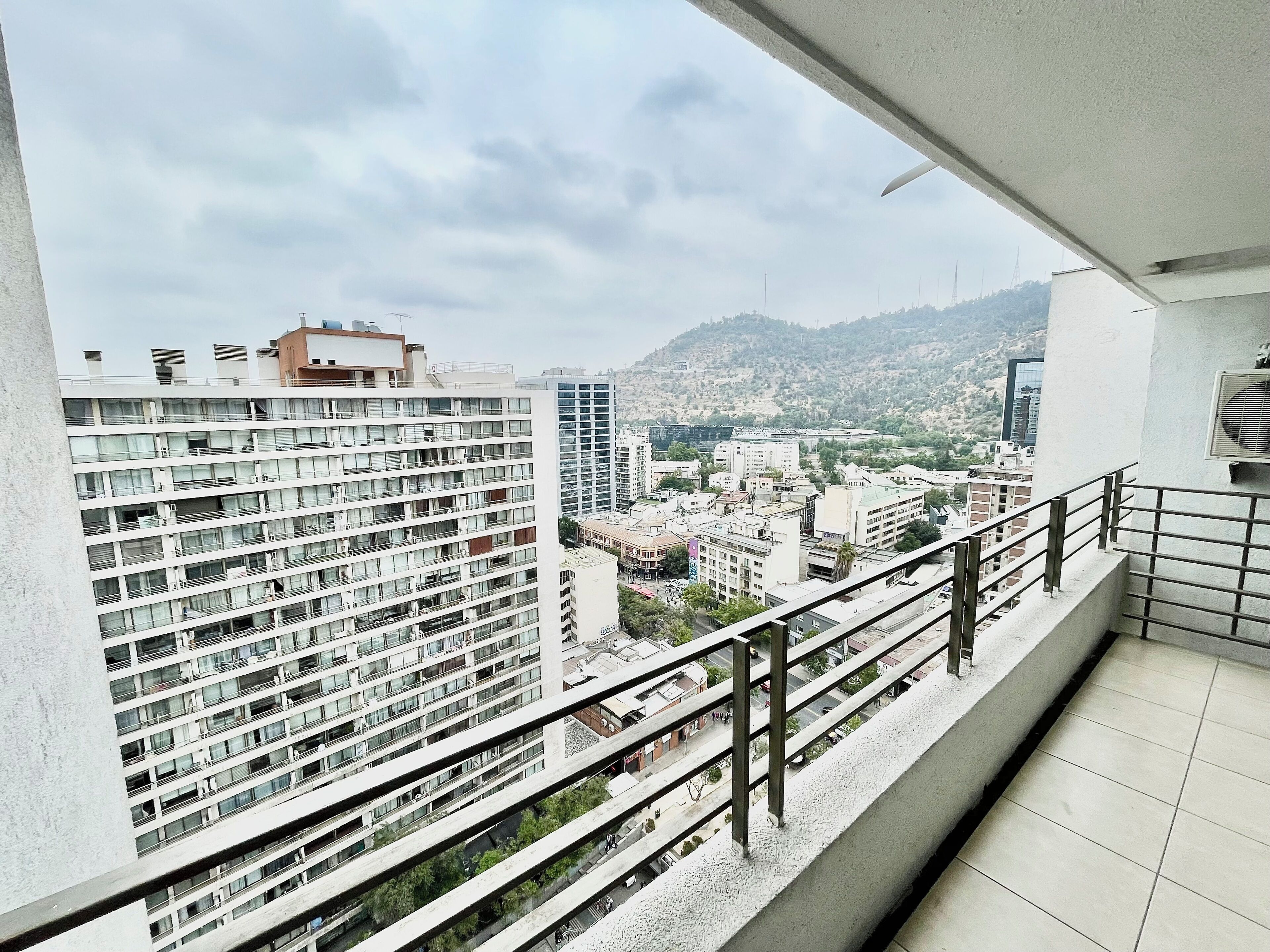 A high-rise building with multiple balconies and a view of a cityscape with other buildings and hills in the background.
