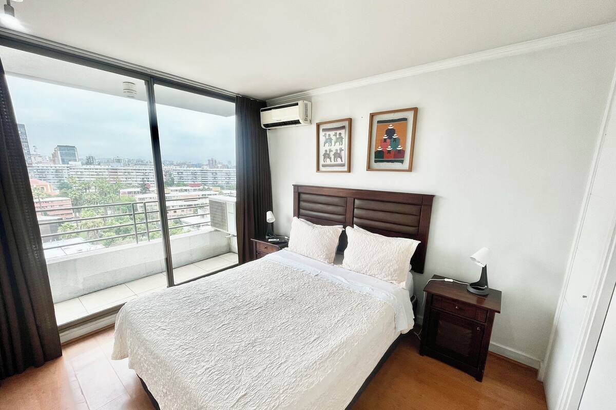 A hotel room with a large bed, a nightstand, a lamp, and two framed pictures on the wall.
