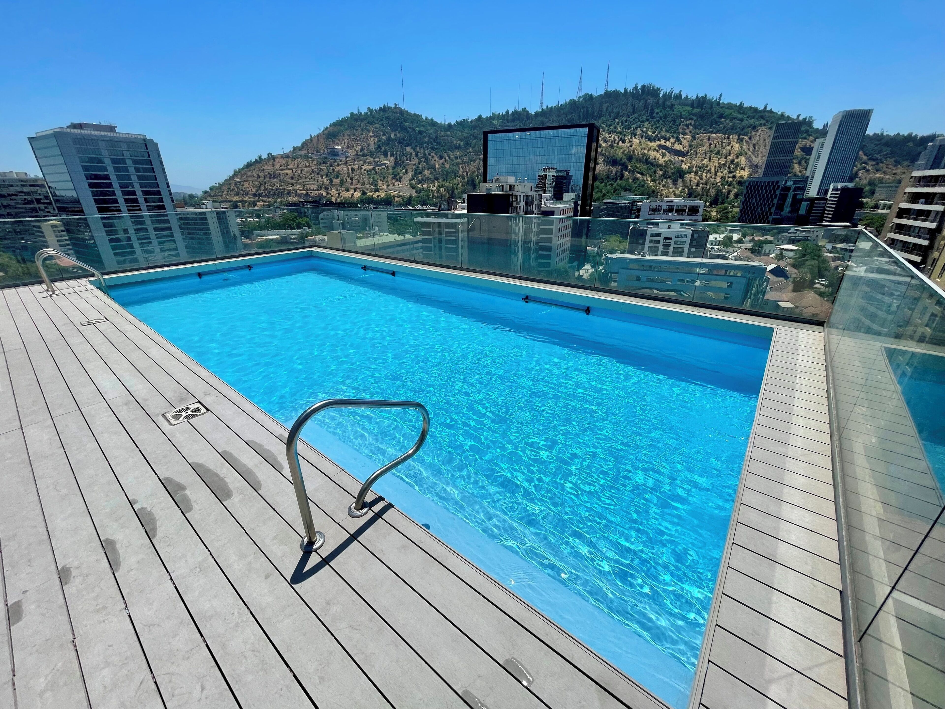 A rooftop pool with a clear view of surrounding buildings and a hilly landscape.