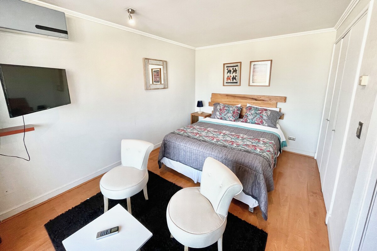 Un dormitorio con una cama, dos sillas, un televisor y una mesita de noche.
