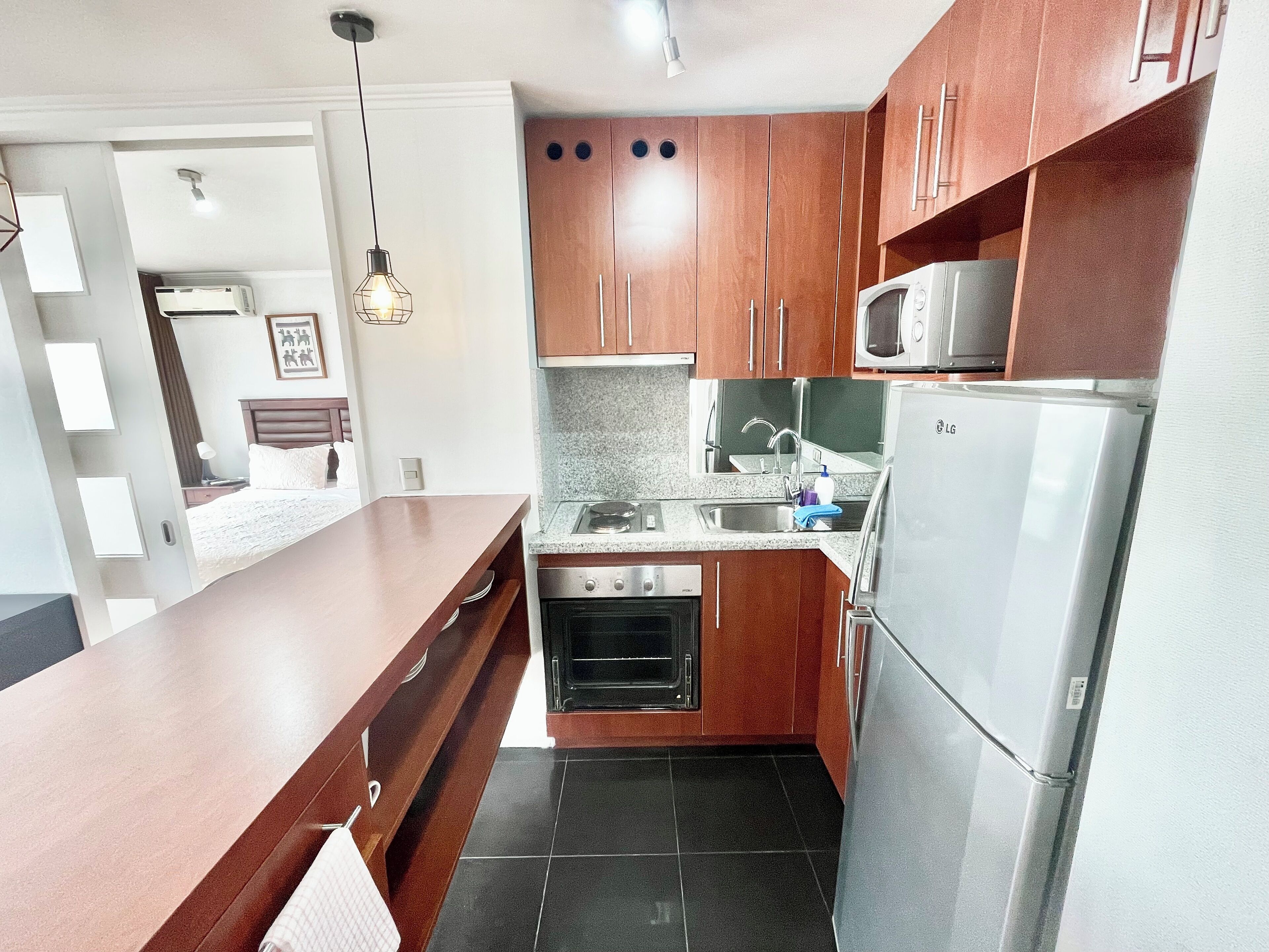 A compact kitchen with wooden cabinets, a stainless steel refrigerator, a microwave, and a gas stove.