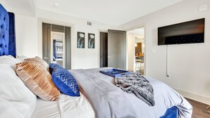 Une chambre d’hôtel moderne dotée d’un grand lit, d’un téléviseur à écran plat fixé au mur et d’une porte donnant accès à une salle de bain.