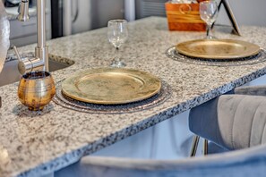 A kitchen counter with a granite top, a sink, a wine glass, and a plate.