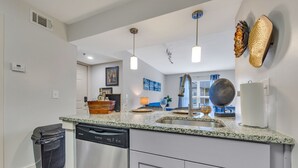 Une cuisine moderne dotée de plans de travail en granit, d’appareils électroménagers en acier inoxydable, de luminaires suspendus et d’œuvres d’art décoratives murales.