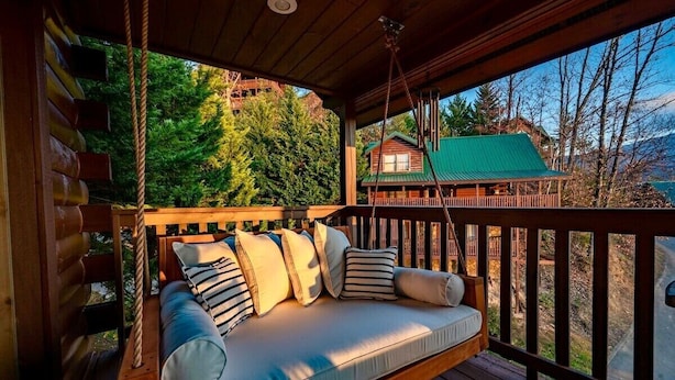 Una terraza de madera con un asiento columpio y una cabaña al fondo.