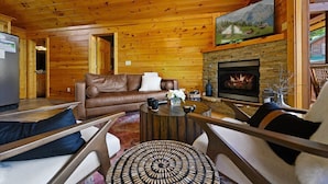 Interior acogedor de una cabaña con chimenea, paredes de madera, un sofá de cuero y un televisor montado encima.