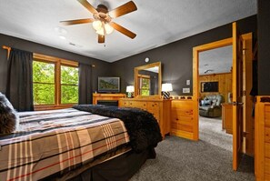 A bedroom with a bed, a wooden dresser, a ceiling fan, and a large window.