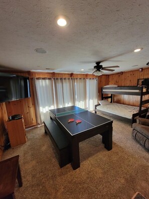 Une pièce équipée d’une table de ping-pong, de lits superposés, d’un téléviseur et d’un ventilateur de plafond.