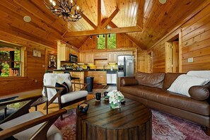 A wooden cabin interior with a living room, kitchen, and dining area.