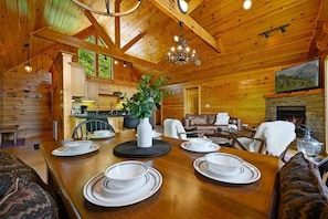 A wooden cabin interior with a dining table set for four, a fireplace, and a cozy living area.