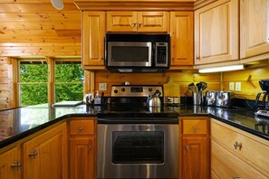 Une cuisine dotée de meubles en bois, d’une cuisinière en acier inoxydable, d’un four à micro-ondes et d’une fenêtre donnant sur un paysage verdoyant.