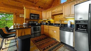A wooden cabin kitchen with a central island, stainless steel appliances, and a large window overlooking greenery.