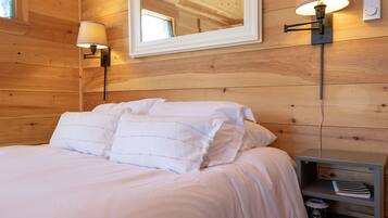 A wooden-paneled bedroom with a bed, two wall-mounted lamps, a mirror, and a nightstand with a lamp and a kettle.