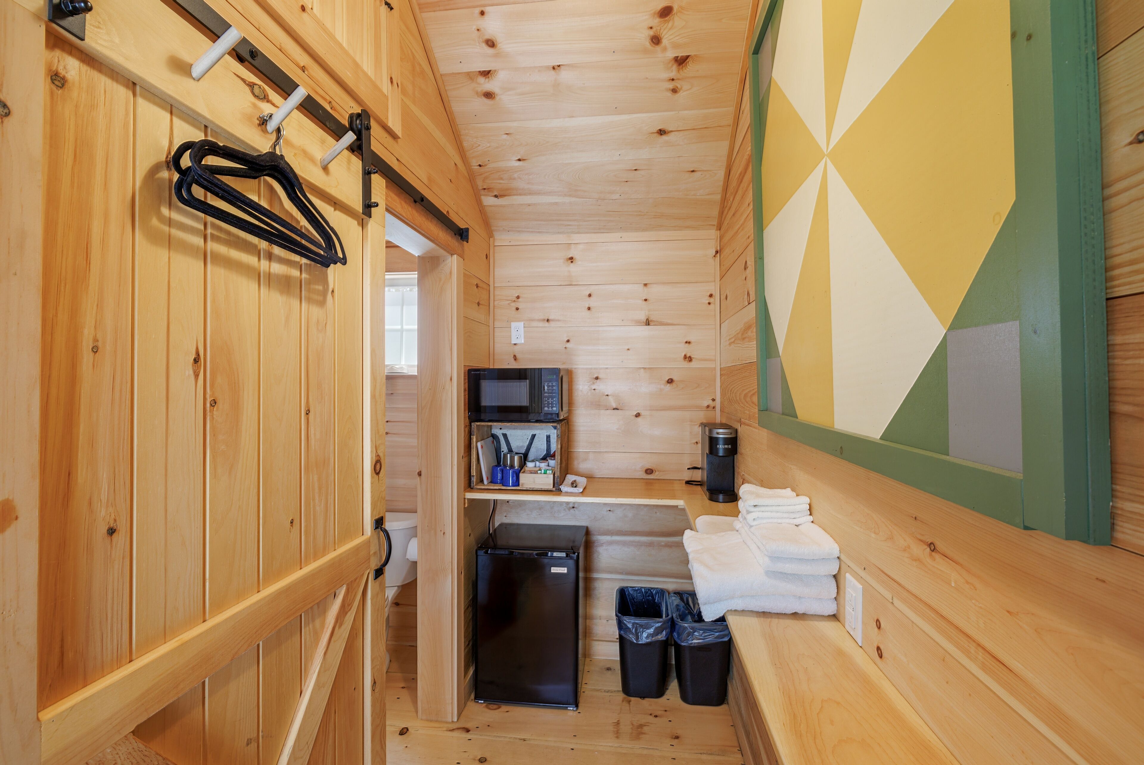 Una cabaña de madera pequeña con kitchenette, microondas, cafetera y basurero.