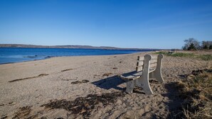 A beach with a single wooden bench facing the water. - Cabin 1 Near Sandy Point Beach + Wood-Fired Sauna (Stockton Springs)