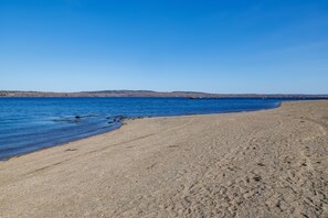 Uma extensa praia de areia com águas azul-claras e colinas ao longe.