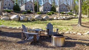 A cabin with a stone fireplace, Adirondack chairs, and a large rock garden. - Cabin 1 Near Sandy Point Beach + Wood-Fired Sauna (Stockton Springs)