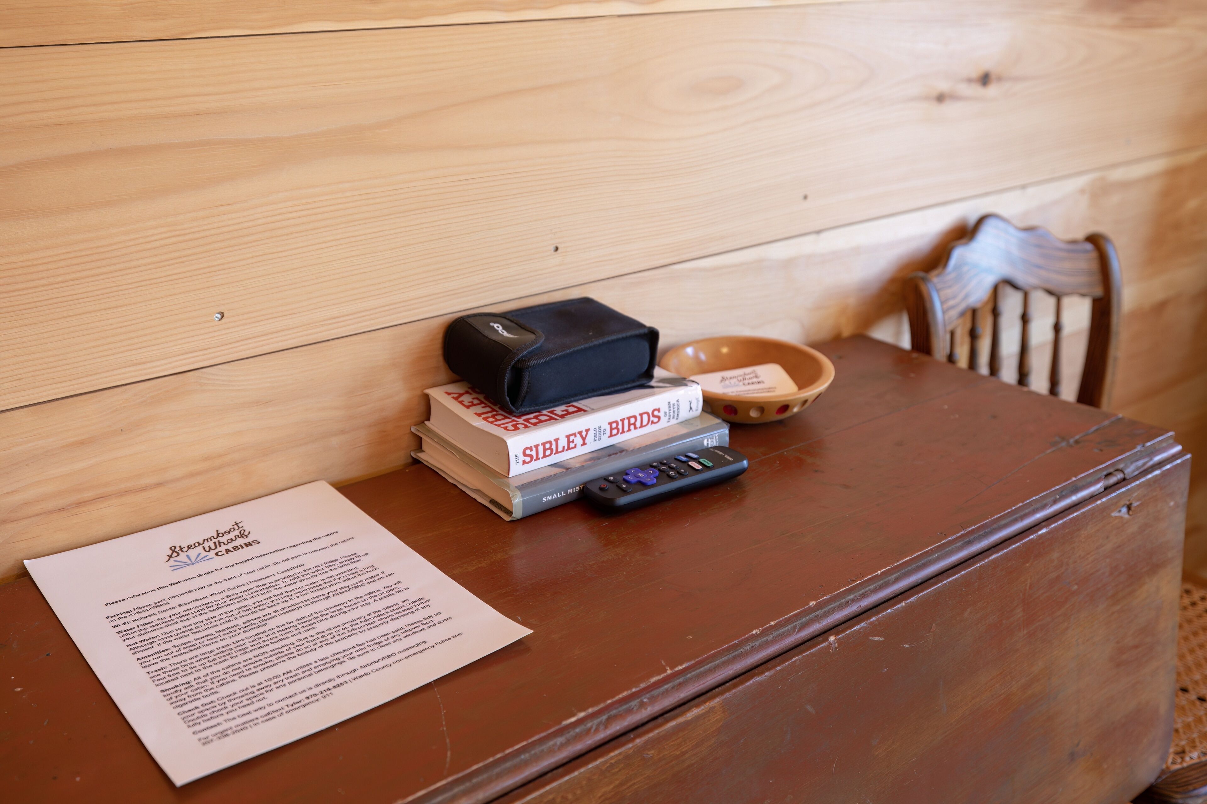 Ein Holztisch mit einer Bücherstapel, einer Fernbedienung, einer Schale und einer Speisekarte.