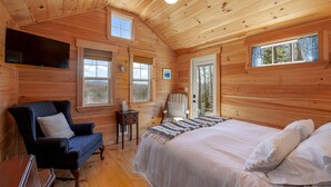 A wooden cabin bedroom with a bed, a chair, a small table, and a television. - Cabin 1 Near Sandy Point Beach + Wood-Fired Sauna (Stockton Springs)