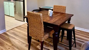 Ein Essbereich mit Holztisch und gewobenen Stühlen, einer Chandelierleuchtre und einer Küche im Hintergrund.