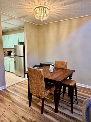 Ein Essbereich mit Holztisch und gewobenen Stühlen, einer Chandelierleuchtre und einer Küche im Hintergrund.