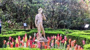 Eine Statue in einem Garten mit ordentlich geschnittenen Hecken und bunten Blumen.