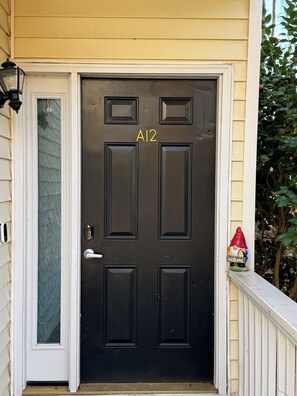 Une porte d’entrée noire avec une plaque portant le numéro « A12 » et un petit panneau d’accueil orné d’une figurine de gnome.
