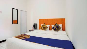 A hotel room with a bed, a wooden headboard, a desk with a chair, and a mirror on the wall.