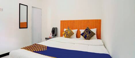 A hotel room with a bed, a wooden headboard, a desk with a chair, and a mirror on the wall.