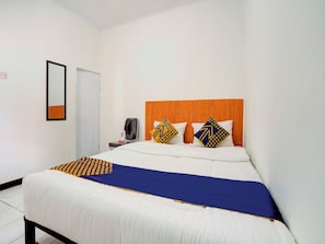 A hotel room with a bed, a wooden headboard, a desk with a chair, a mirror, and a wall socket. - Spot ON 90200 Pondok Sabaraya Cileunyi Syariah (Cileunyi)