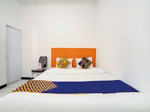 A hotel room with a wooden headboard, a bed with white and blue bedding, two pillows with geometric patterns, a small table with a chair, and a whiteboard on the wall. - Spot ON 90200 Pondok Sabaraya Cileunyi Syariah (Cileunyi)
