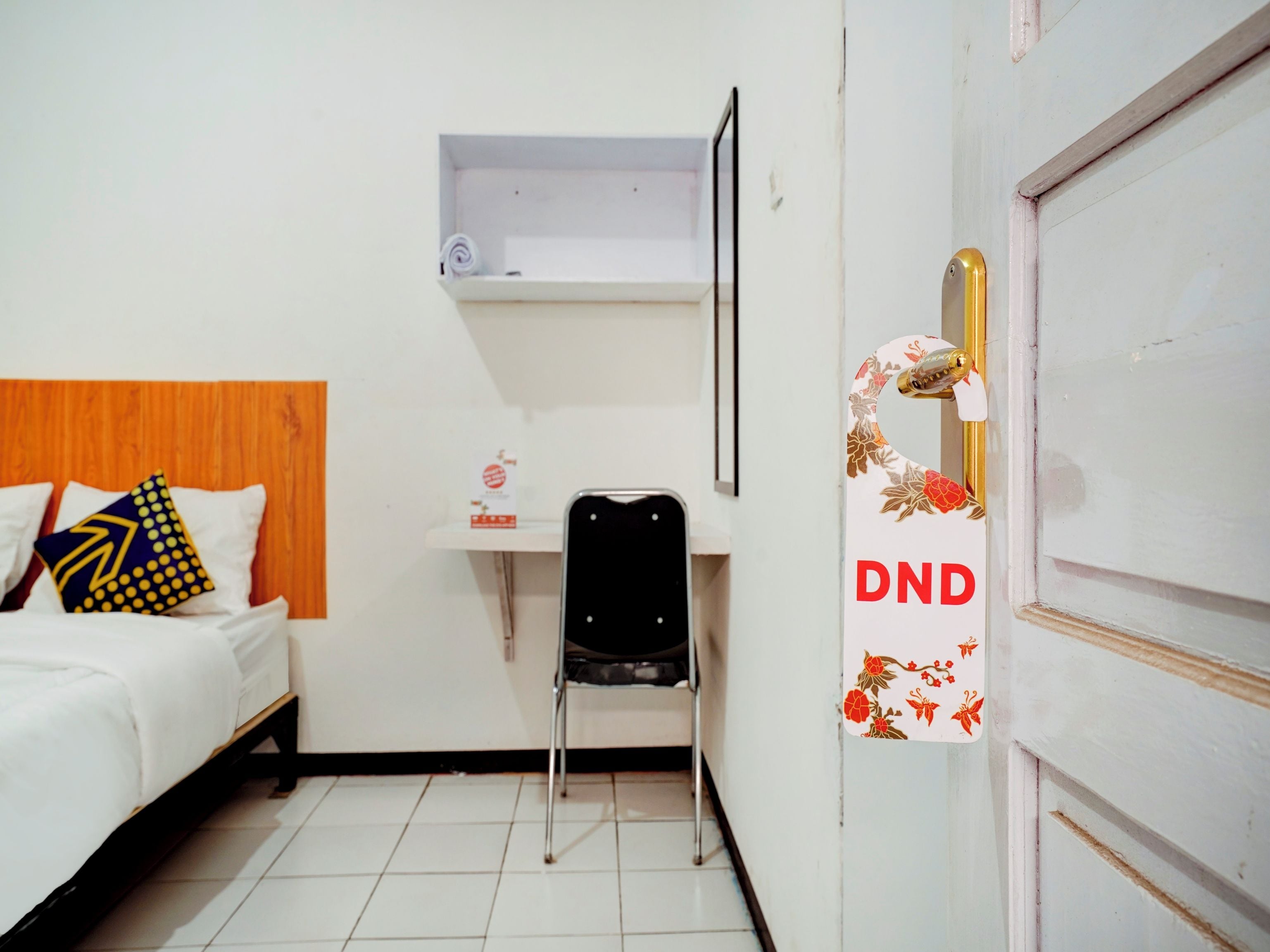 A hotel room with a bed, a chair, a desk, and a door with a DND sign.