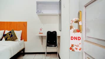Quarto de hotel com cama, cadeira, escrivaninha e porta com placa de 'Não Perturbe'.