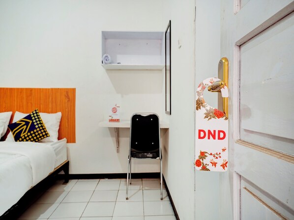 A hotel room with a bed, a chair, a desk, and a door with a DND sign.
